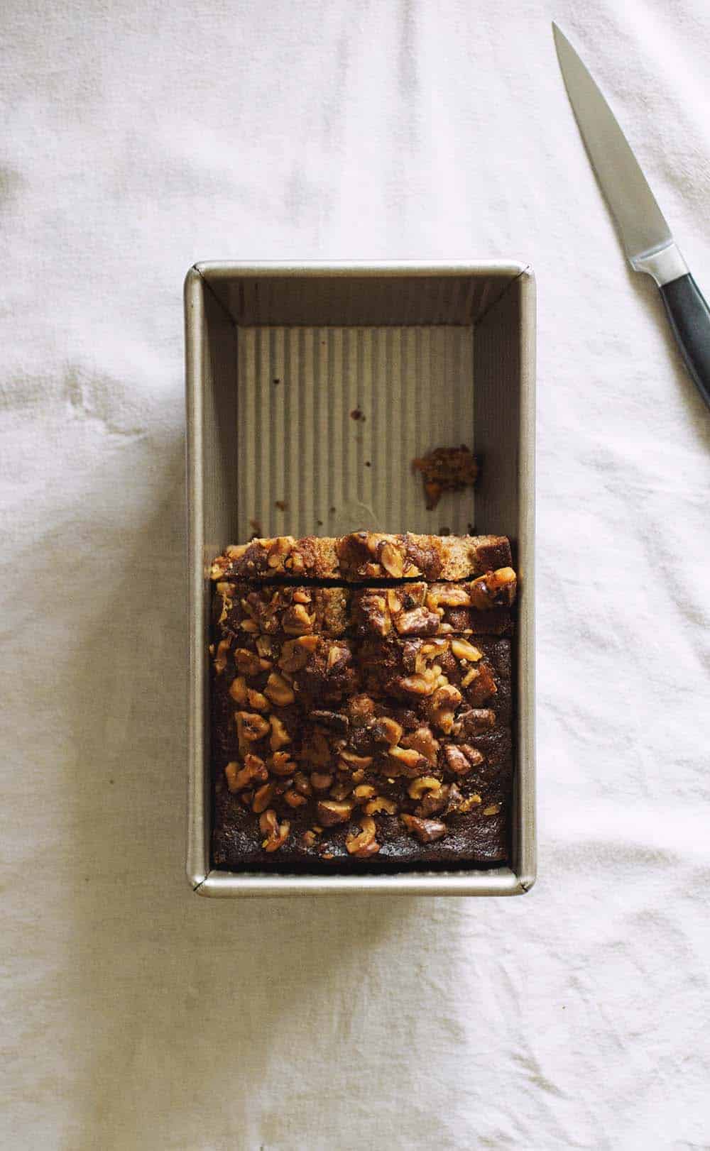 A loaf pan half full of nut-topped banana bread.