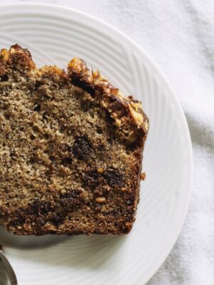 A close up on a half slice of chocolate chip banana bread on a white plate.