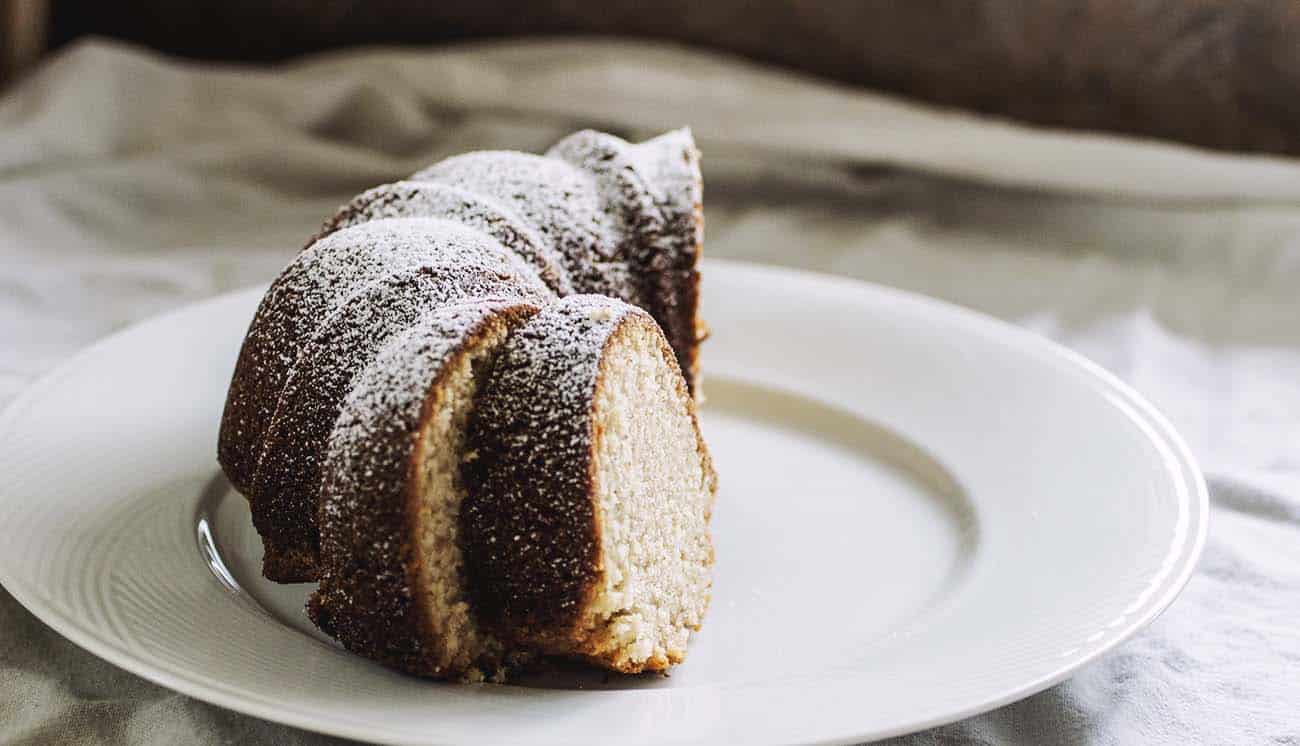 Half a bundt cake topped with powdered sugar on a white plate with berries.