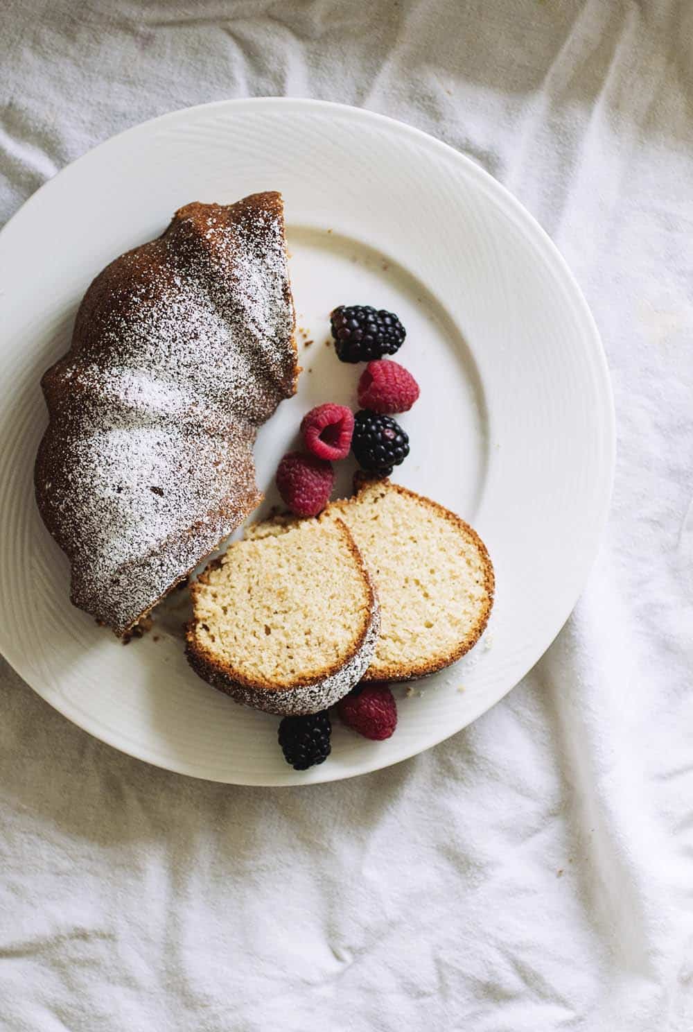 Half a bundt cake topped with powdered sugar on a white plate with berries.