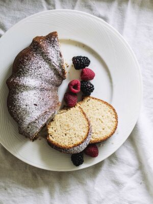Half a bundt cake topped with powdered sugar on a white plate with berries.