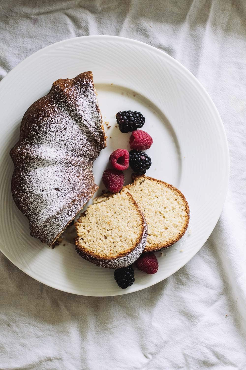 Half a bundt cake topped with powdered sugar on a white plate with berries.