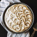 A toasted lemon meringue tart on a blue and white striped towel on a black table.