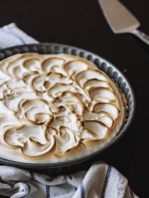 A toasted lemon meringue tart on a blue and white striped towel on a black table.