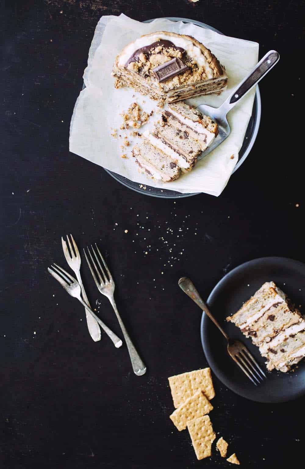 Slices of s\'mores layer cake on black plates with several forks lying on a black table.