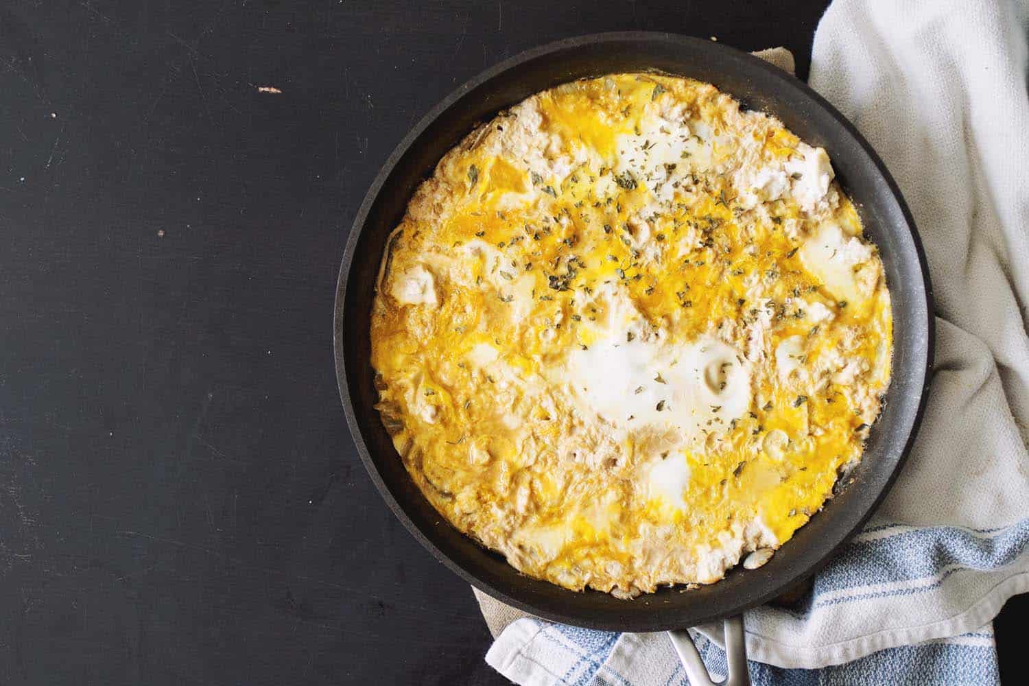 A black pan filled with a mixture of eggs, tofu and onions.