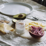 Half a pomegranate on a cutting board with cheese, salt and half an avocado.
