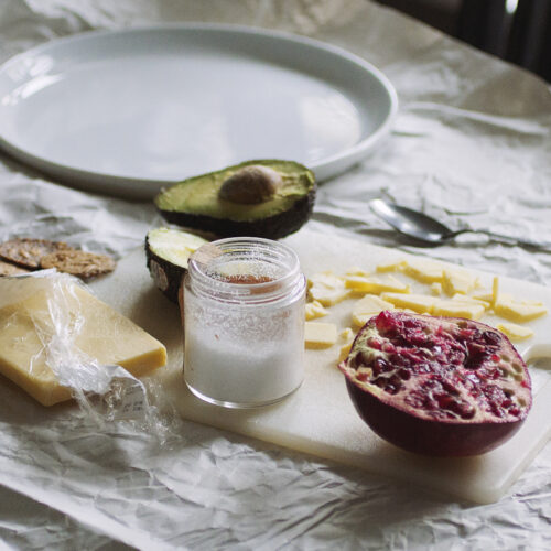 Half a pomegranate on a cutting board with cheese, salt and half an avocado.