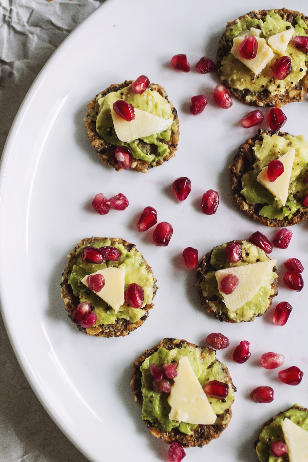 Crackers topped with avocado, cheese and pomegranate seeds.