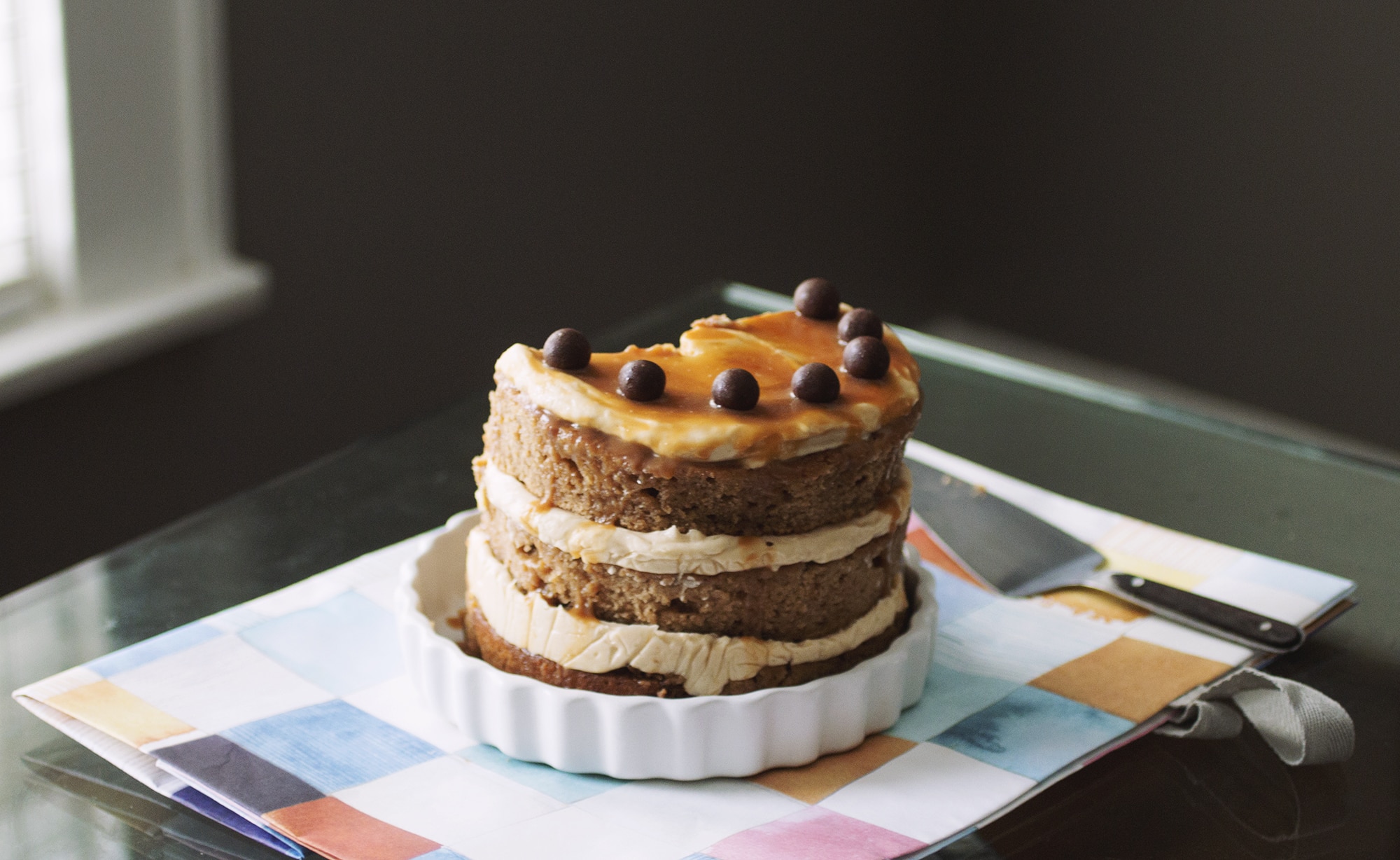 3/4 of a caramel apple cake topped with chocolate balls on a white plate.