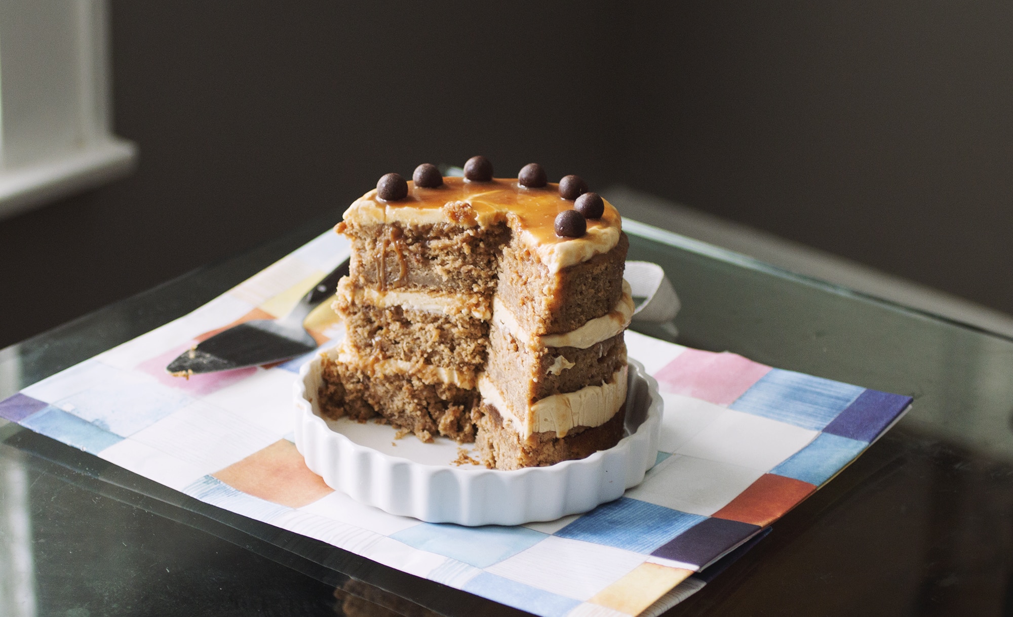 3/4 of a caramel apple cake topped with chocolate balls on a white plate.
