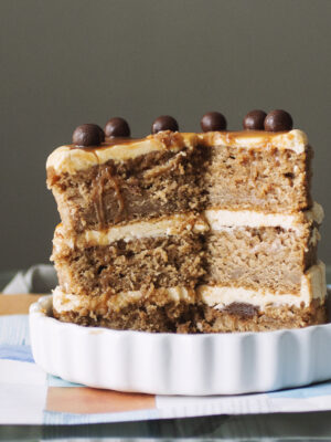 3/4 of a caramel apple cake topped with chocolate balls in a white plate.