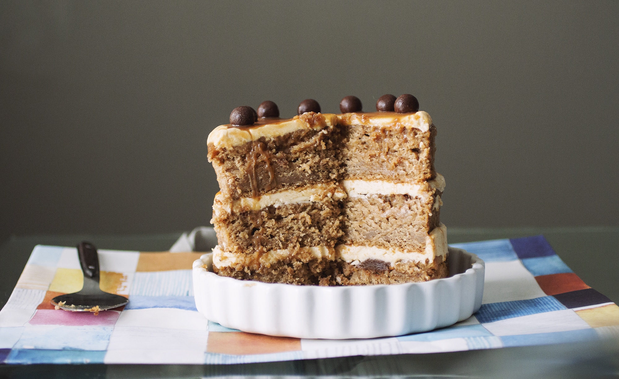 3/4 of a caramel apple cake topped with chocolate balls in a white plate.