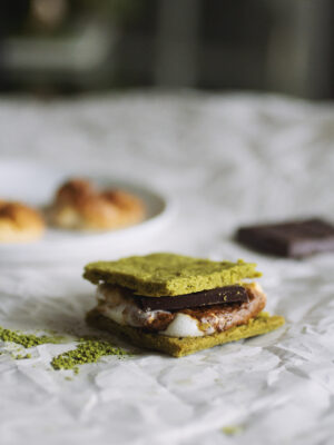 A matcha s'more with chocolate and toasted marshmallows in the background.