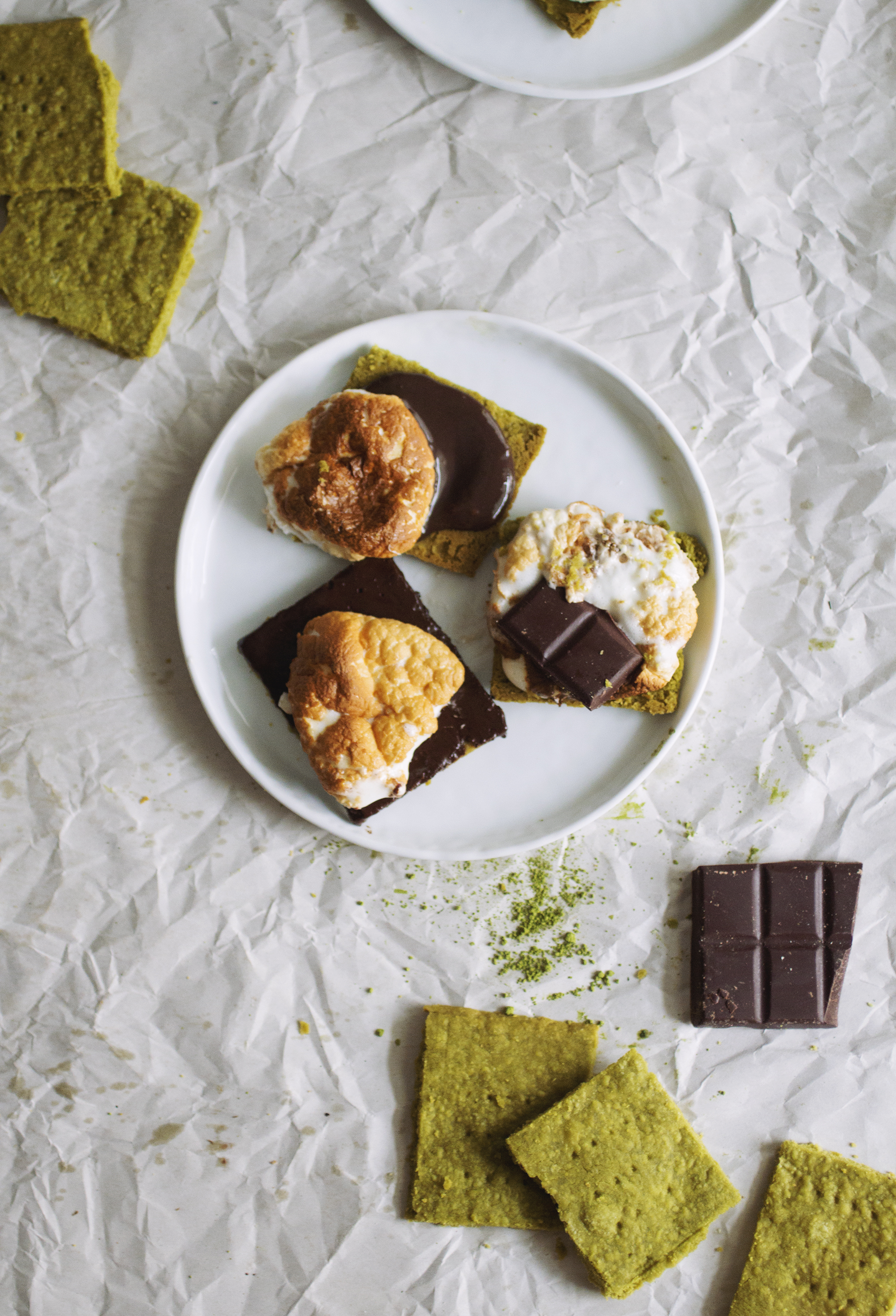 3 matcha s\'mores on a white plate with squares of matcha graham crackers in the background.