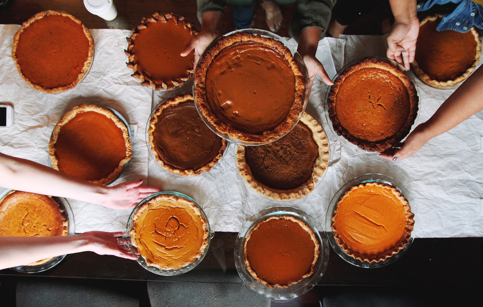 One person holding up a pumpkin pie above a table filled with pumpki pie.