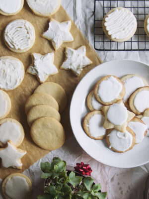A bowl full of sugar cookies next to a parchment paper topped with more frosted sugar cookies.