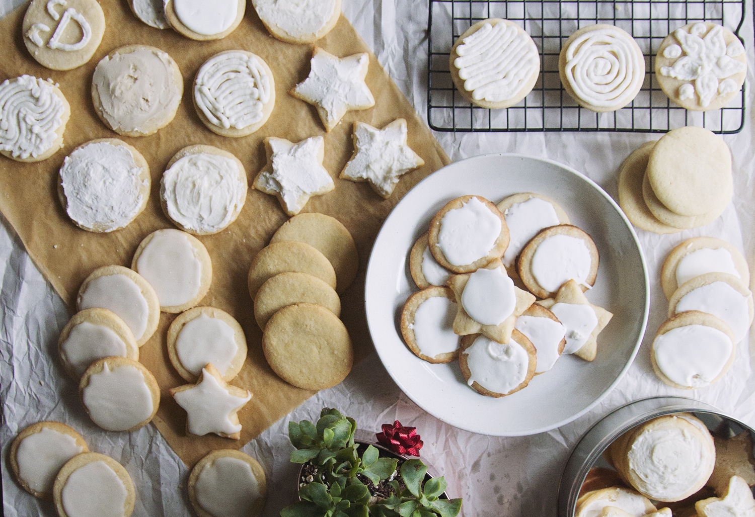 A bowl full of sugar cookies next to a parchment paper topped with more frosted sugar cookies.