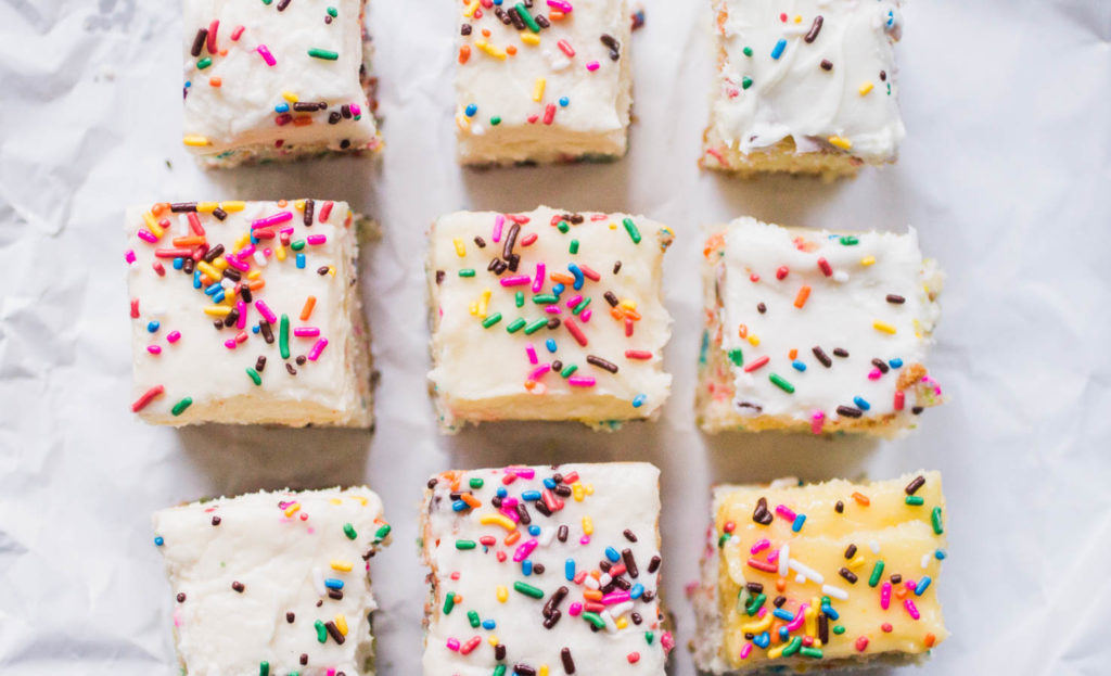 Nine slices of sprinkle cake lined up on white parchment.