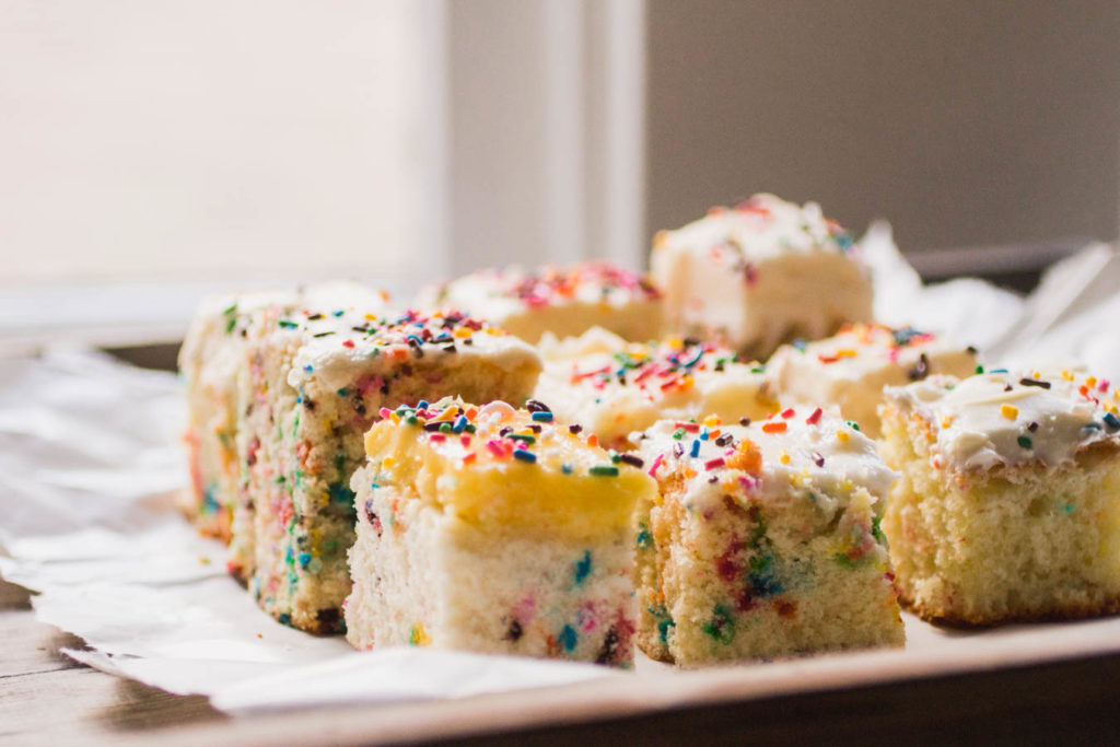 Side view of several slices of different sprinkle cake recipes on white parchment.