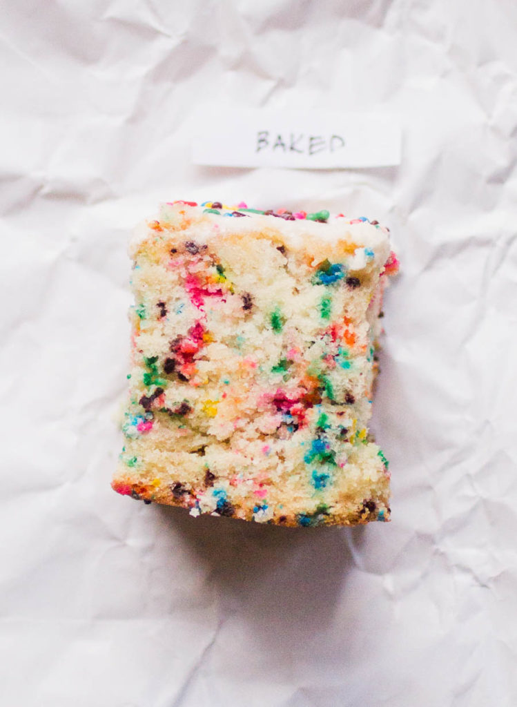 Single slice of Baked sprinkle cake recipe on white parchment paper.