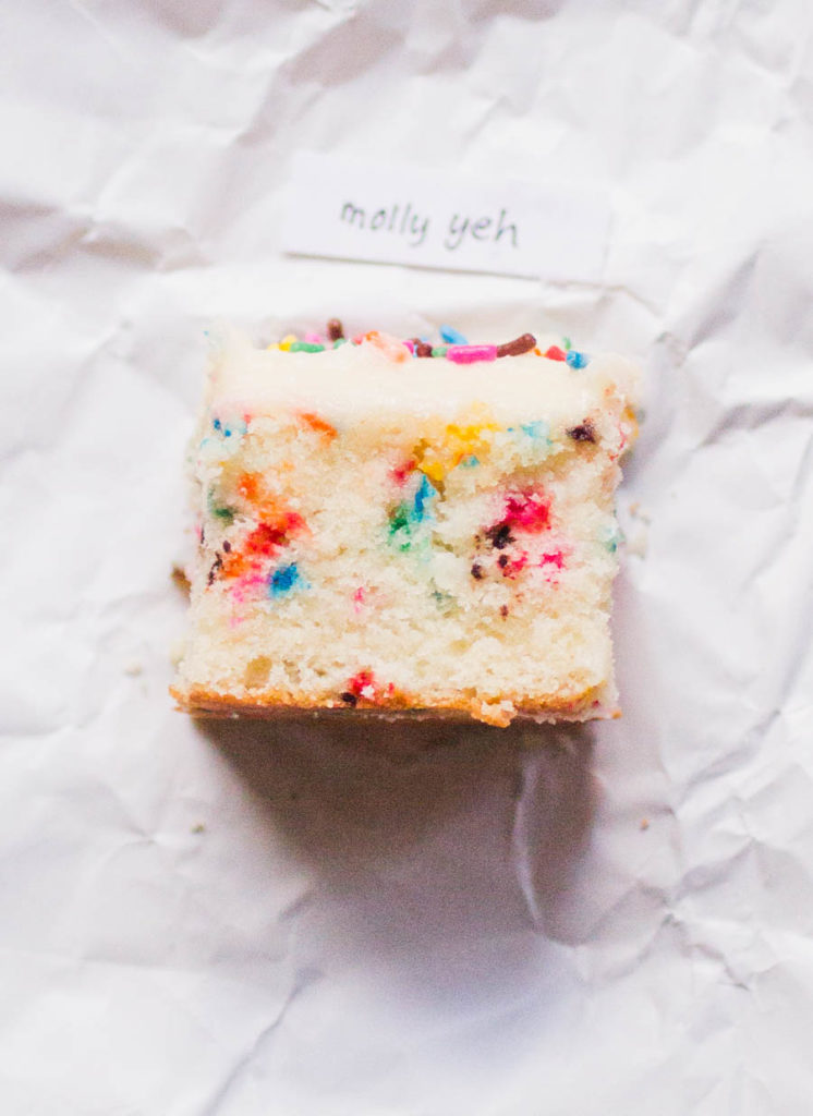 Single slice of Molly Yeh sprinkle cake recipe on white parchment paper.