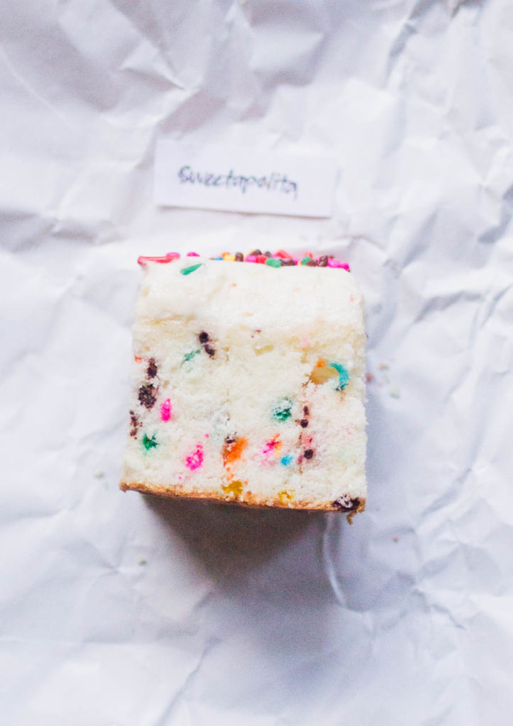 Single slice of Sweetapolita\'s sprinkle cake recipe on white parchment paper.