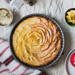 apples arranged in a spiral in a tart pan on a gray background.