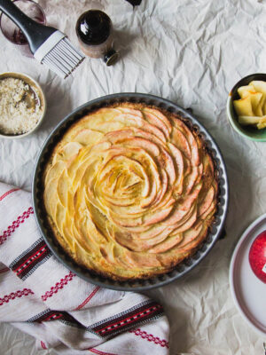 apples arranged in a spiral in a tart pan on a gray background.