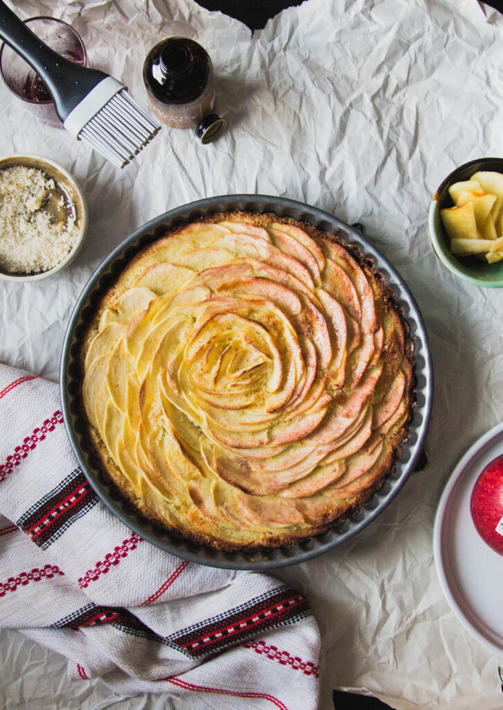 apples arranged in a spiral in a tart pan on a gray background.