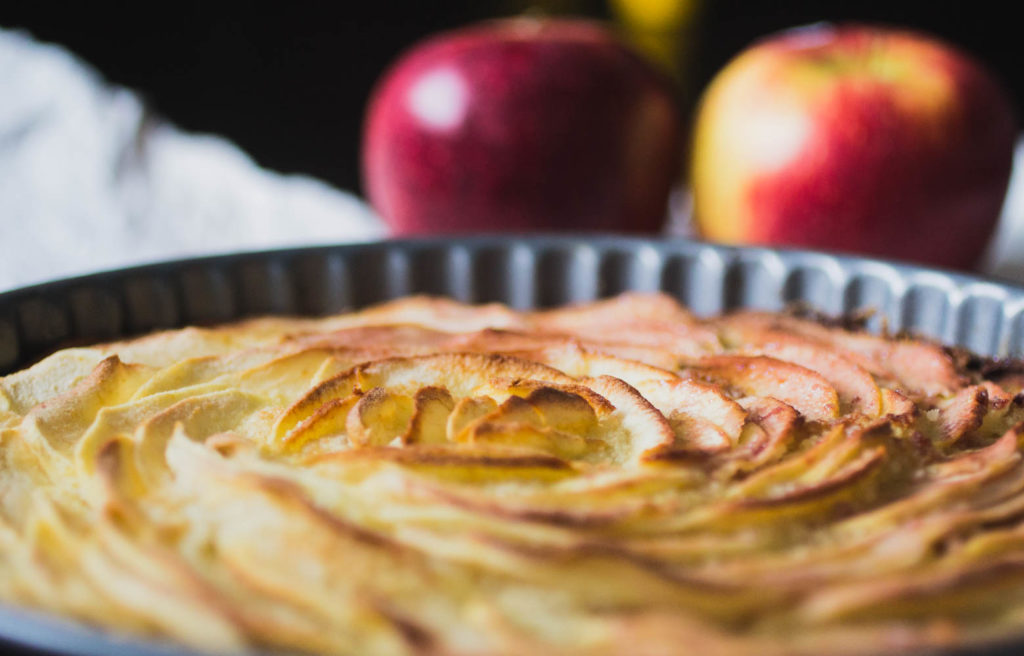 Close up on an apple almond tart with apples in the background.
