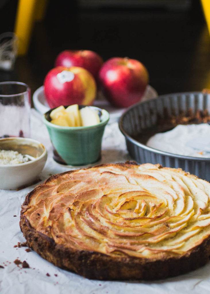 An apple tart with a spiral of apple slices with apples in the background.