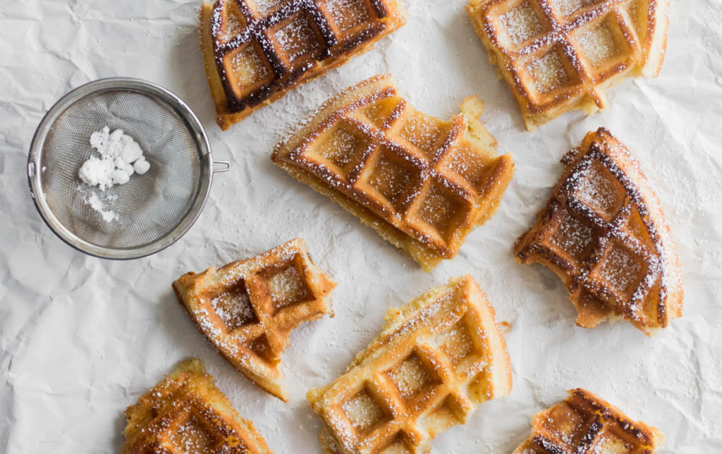 Half eaten Belgian waffle quarters sprinkled with powdered sugar.