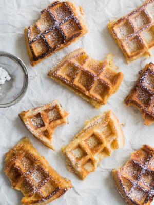 Half-eaten waffles sprinkled with powdered sugar on a white background.