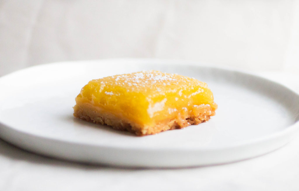 Single slice of new york times lemon bars on white plate.