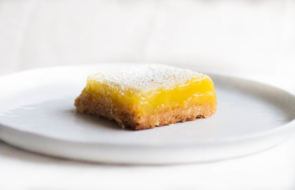 Single slice of cook\'s illustrated lemon bar recipe on ceramic white plate.