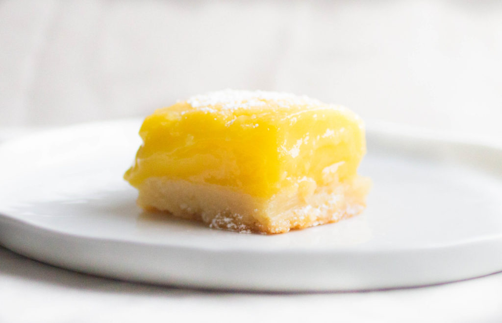 Single slice of Flour bakery lemon bar with bright yellow lemon curd on a white plate.