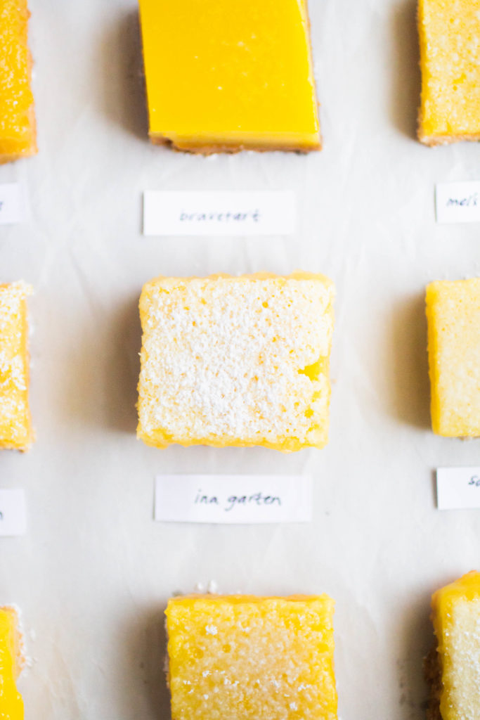 Several slices of different lemon bar recipes on white parchment paper.
