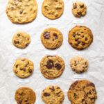 12 different vegan chocolate chip cookie recipes lined up on parchment paper.