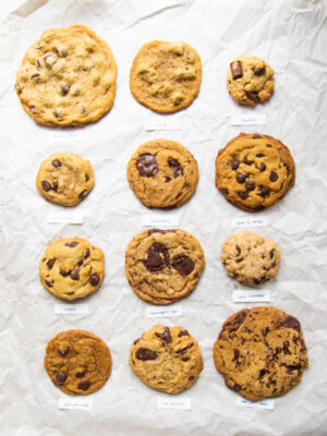 12 different vegan chocolate chip cookie recipes lined up on parchment paper.