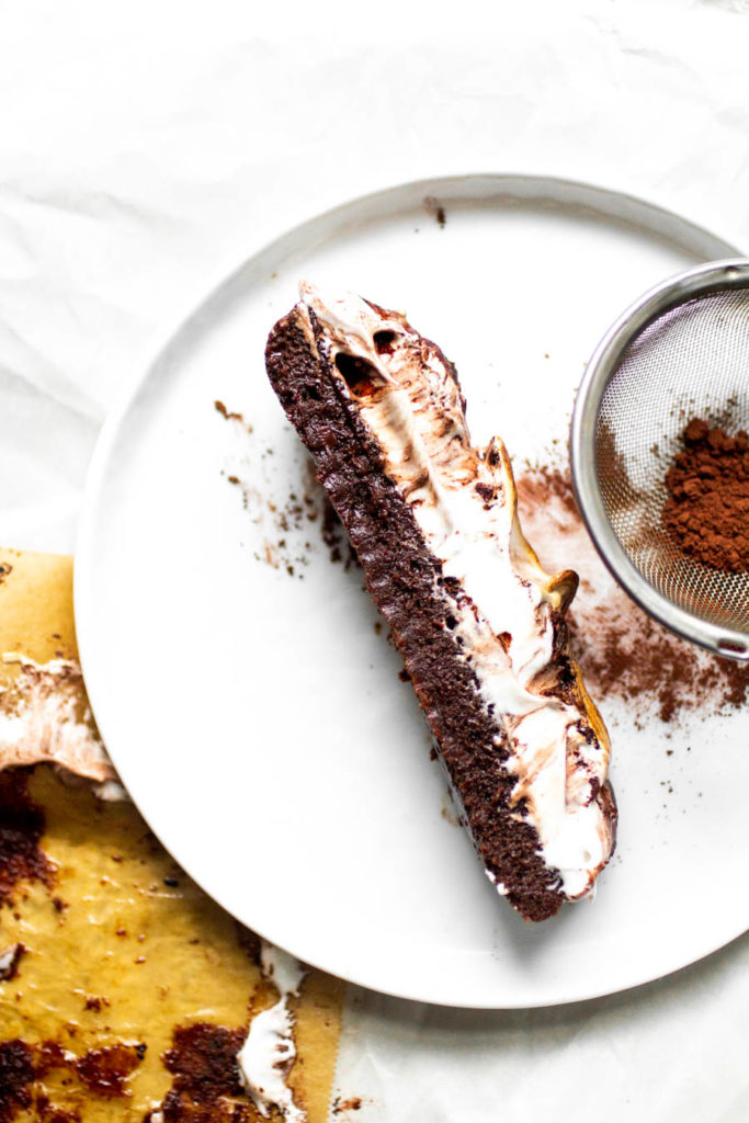 A long, thin slice of flourless chocolate cake topped with toasted meringue on a white plate.