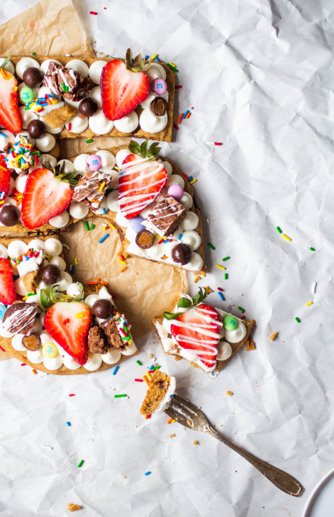 A slice taken out of a birthday cookie cake shaped like the numbers 35 topped with frosting, fruit and candy.