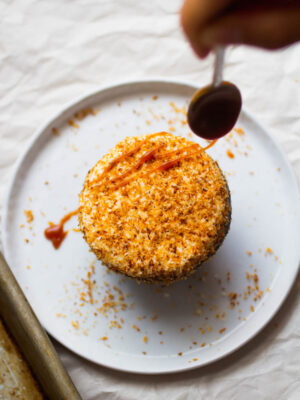 A spoon drizzling caramel on top of a coconut-topped cupcake.