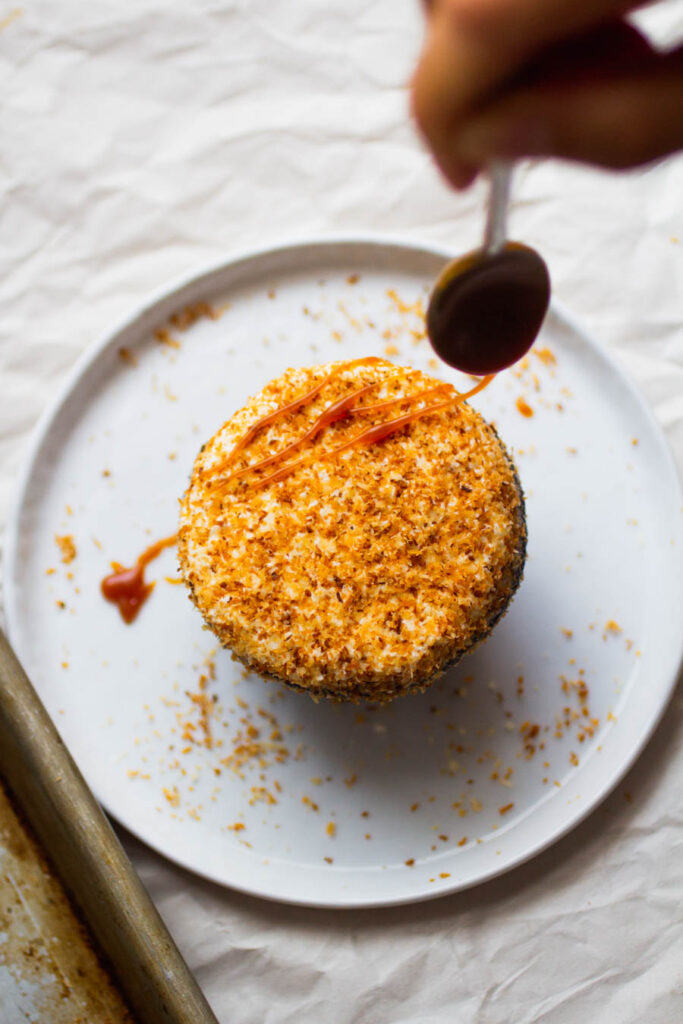 A spoon drizzling caramel on top of a coconut-topped cupcake.