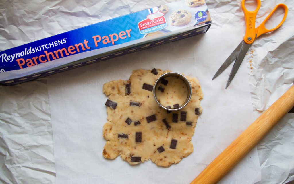 Cookie dough rolled out on parchment paper with a round cookie cutter.