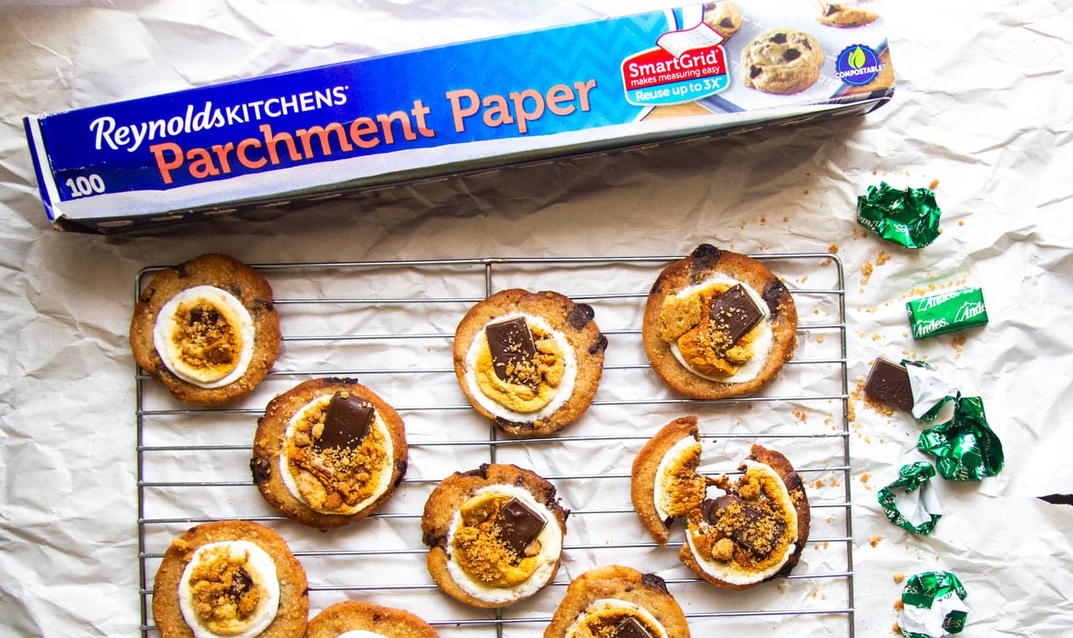 Baked s\'mores cookies on cooling racks next to a roll of Reynolds Kitchens parchment paper.