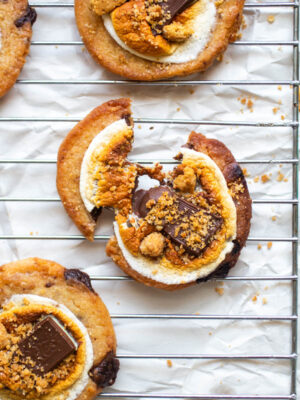 A smore's cookie broken in half on a wire baking rack.