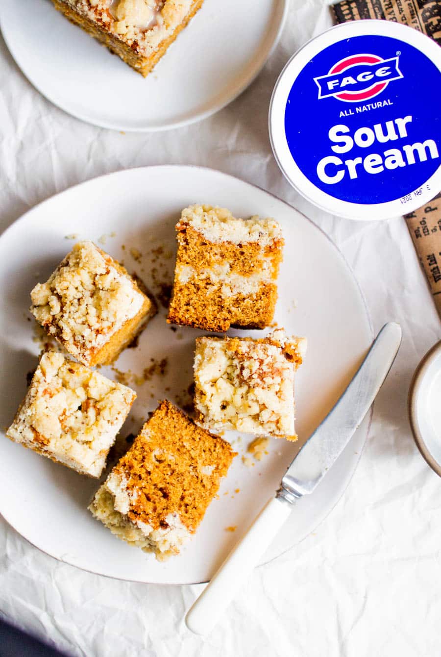 Several slices of gingerbread coffee cake on a white plate next to a container of Fage sour cream.