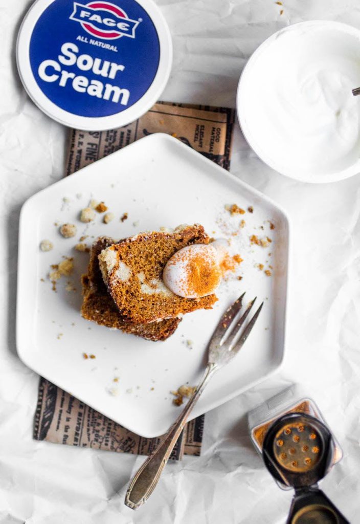 A slice of gingerbread coffee cake on a white plate with a fork and a dollop of Fage sour cream.