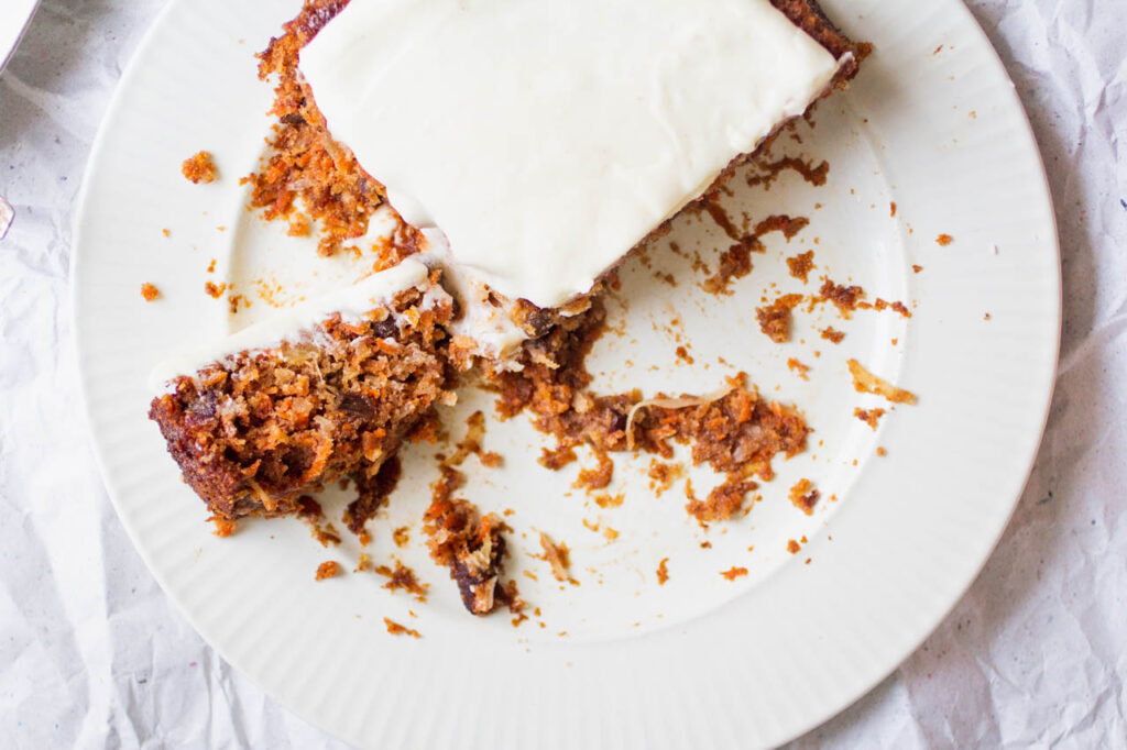 A quarter of a carrot cake left on a white plate.
